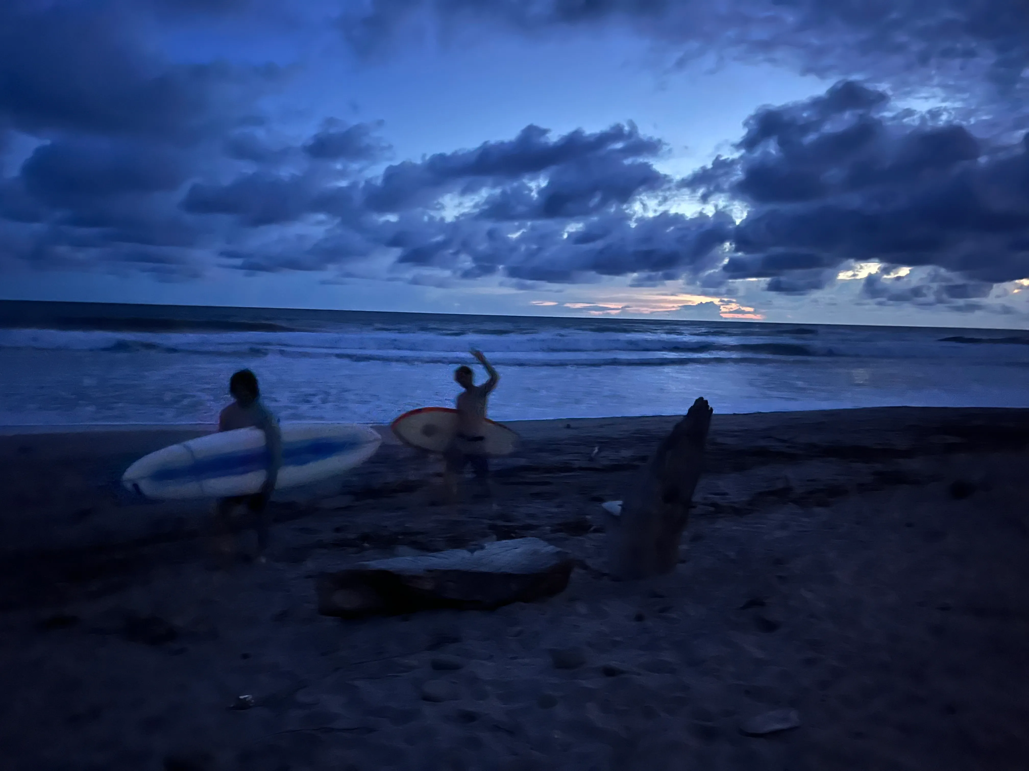 Surfers carrying their boards beside the ocean at dusk